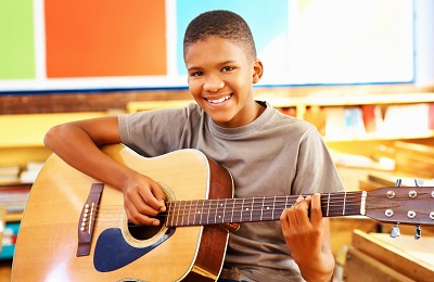 child with a smile holding a guitar.